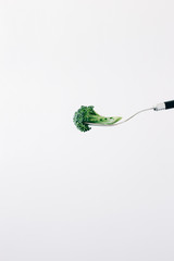 a fork with a green inflorescence of fresh broccoli on a white background. vegan food