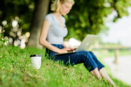Coffee break on fresh air concept. Caffeine power of nature. Energy charge and refreshment. Coffee cup take away close up shot. Coffee cup on green grass woman worker with laptop defocused background