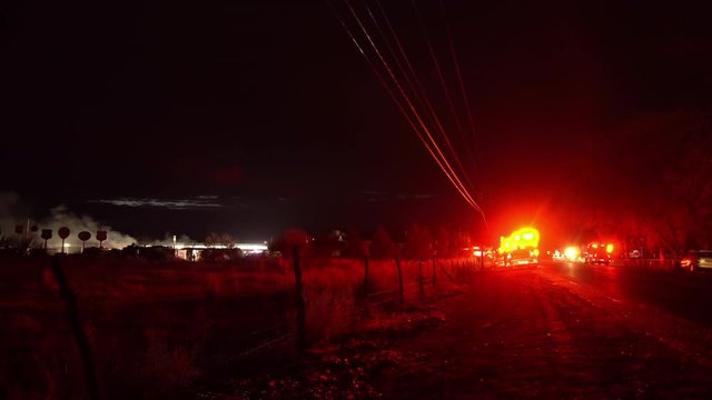 Emergency lights flashing as firefighters respond to small fire burning at night.