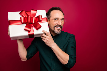 Photo of cheerful positive handsome attractive man looking at giftbox held with hands in spectacles isolated curiously over bright color background