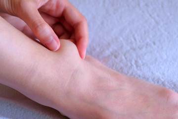 Woman palpates hand leg ankle hygroma in joint, foot closeup view on white background. Tumor, inflammation of the ankle joint of left leg. Trauma, shock, swelling of internal tissues. Joint disease.