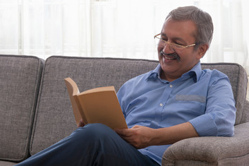 Portrait of a senior man sitting at home and reading a book. - Powered by Adobe