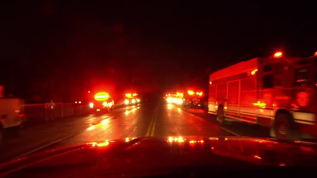 Driving past lights flashing on emergency vehicles with firetrucks and ambulances lined up on both side of the road as they respond to small fire.