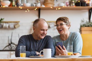 Senior couple eating breakfast and using smartphone at home