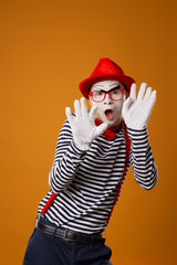 Fototapeta na wymiar Serious mime in white gloves and red hat looking at camera on orange background