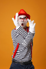 Young mime male in white gloves and red hat looking at camera on orange background
