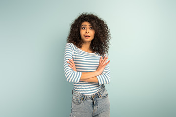 skeptical mixed race girl looking at camera while standing with crossed arms on grey background