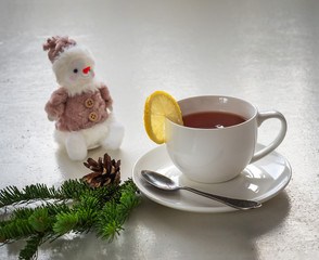 Obraz na płótnie Canvas On a rustic table with spruce twigs and a cone, a pink snowman stands near a mug of tea and lemon
