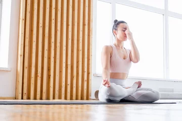  Side view of young healthy woman sitting in lotus mudra alternate nostril breathing exercise, nadi shodhana pranayama pose in spacious gym. Concept of breathing practice and meditation. Copyspace © Rithor