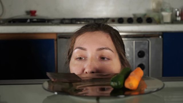 girl peeks out from table in search of food and takes chocolate bar from plate breaking healthy eating closeup