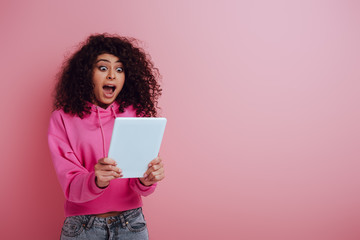 shocked bi-racial girl looking at digital tablet on pink background