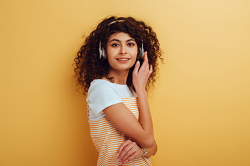 smiling bi-racial girl in wireless headphones looking at camera on yellow background