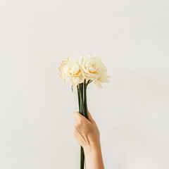 Female hand hold narcissus flowers bouquet on white background. Flat lay, top view minimal floral composition.