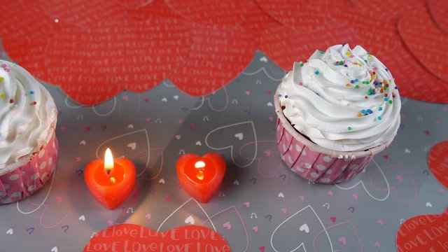 Top view shot of valentine's cupcakes with burning candles - romantic love concept. Pan shot of beautiful Valentine's day party table with frosted cupcakes and scented heart-shaped candles - celebr...