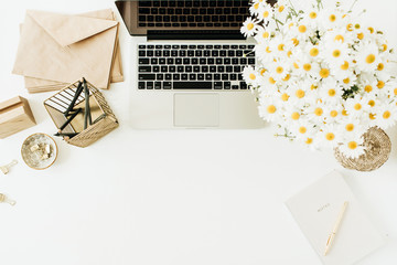 Home office desk workspace with laptop, chamomile daisy flowers bouquet and notebook on white background. Flat lay, top view minimal hero header with copy space mockup.