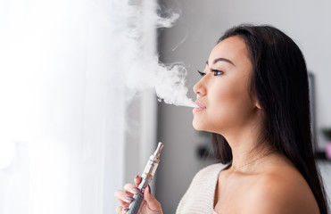 Casual asian woman vaping electronic cigarette at home
