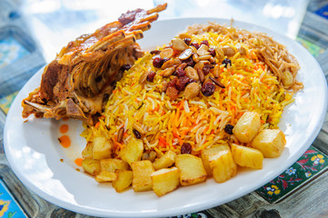 Plate of yellow rice topped with mutton meat and potatoes.