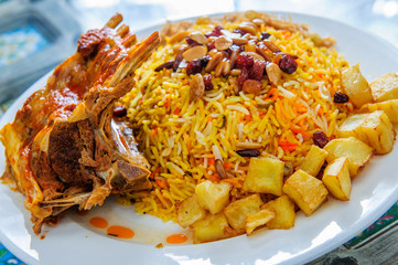 Plate of yellow rice topped with mutton meat and potatoes.