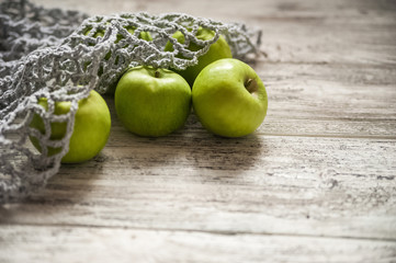 Mesh bag full of colorful apples from the garden, on gray wood background. Fresh apples in a mesh bag, top view. Ripe apples in a beautiful trendy gray cotton string bag, eco-friendly packaging, zero 