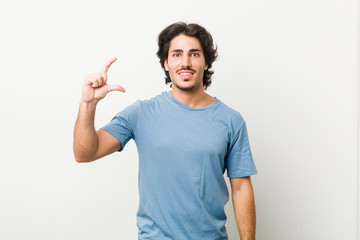 Young handsome man against a white background holding something little with forefingers, smiling and confident.