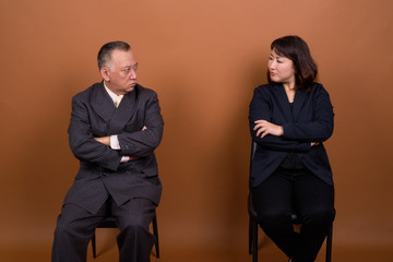 Stressed mature Asian businessman and mature Asian businesswoman looking at each other