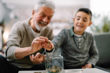 Grandpa and grandson saving money. Grandfather teaching grandchild how to save money.  