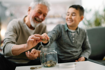 Grandpa and grandson saving money. Grandfather teaching grandchild how to save money.  