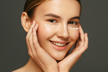 Face skin care. Beautiful young woman with anti age eyes cream on her face. Beauty treatment and...