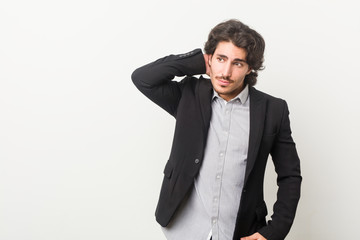 Young business man against a white background touching back of head, thinking and making a choice.