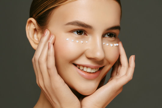 Face skin care. Beautiful young woman with anti age eyes cream on her face. Beauty treatment and spa concept.