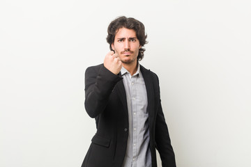 Young business man against a white background showing fist to camera, aggressive facial expression.