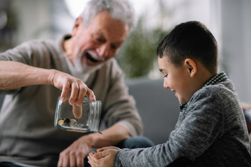 Grandpa and grandson saving money. Grandfather teaching grandchild how to save money.  