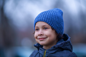 Curly boy on blue knitted hat looks away