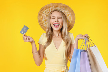 Excited screaming young woman holding shopping bags and credit card standing isolated over yellow...