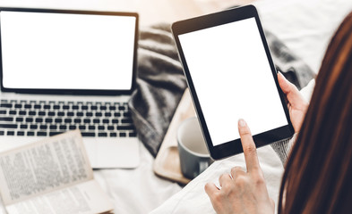 Woman relaxing and using digital tablet computer with white mockup blank screens on the bed at home.woman checking social apps and working.Communication and technology concept