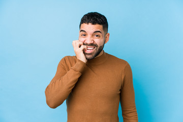 Young latin man against a blue  background isolated biting fingernails, nervous and very anxious.