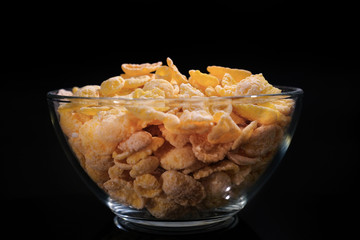 Cornflakes in a glass plate on a black background.