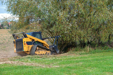  Small excavator destroy trees in field.