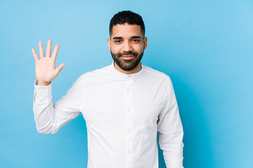 Young latin man against a blue  background isolated smiling cheerful showing number five with fingers.