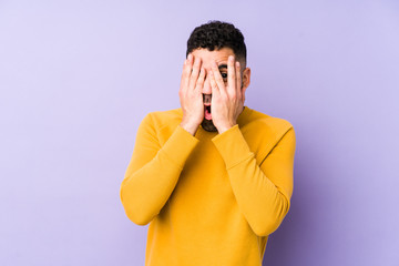 Young mixed race arabic man isolated blink through fingers frightened and nervous.