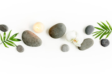 Spa stenen, palmbladeren, bloem witte orchidee, kaars en zen zoals grijze stenen op witte achtergrond. Platliggend, bovenaanzicht