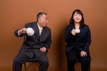 Mature Asian businessman and mature Asian businesswoman drinking coffee together