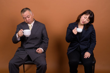 Mature Asian businessman and mature Asian businesswoman drinking coffee together