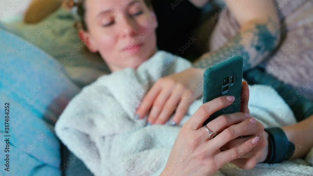 Aufkleber a woman writes a text message on a smartphone while lying in a sofa.