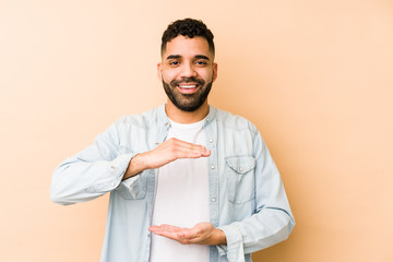 Young mixed race arabic man isolated holding something with both hands, product presentation.