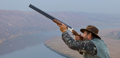 Hunter man in camouflage with a gun during the hunt in search of wild birds or game. Autumn hunting season.