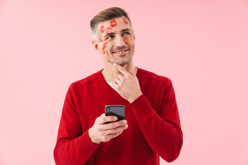 Fototapeta premium Portrait of handsome man with kiss marks at his face holding cellphone
