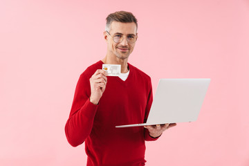 Portrait of handsome man wearing eyeglasses holding laptop and credit card