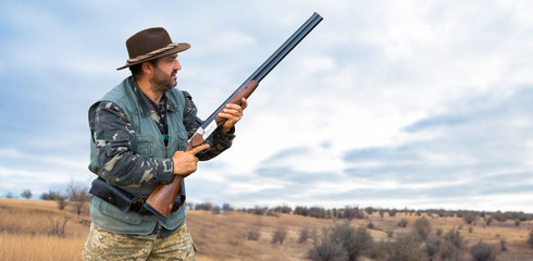 Naklejka premium Hunter man in camouflage with a gun during the hunt in search of wild birds or game. Autumn hunting season.