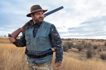 Hunter man in camouflage with a gun during the hunt in search of wild birds or game. Autumn hunting season.